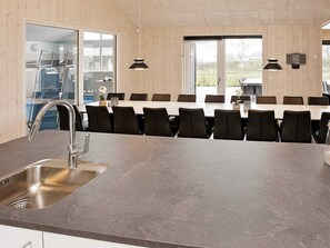 A modern kitchen with a large island, stainless steel sink, and black chairs around a dining table.