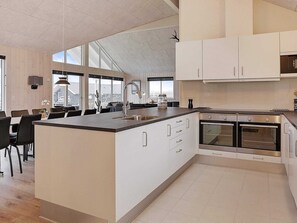 A modern kitchen with a central island, built-in ovens, and a dining area with chairs.