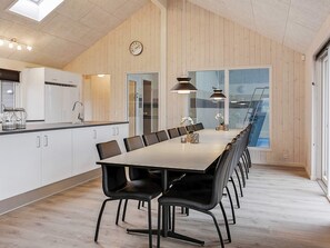 A modern kitchen with a long dining table and chairs, a clock on the wall, and a large window with a view of the outside.
