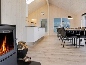 A modern interior with a fireplace, wooden flooring, a dining area with chairs, and a kitchen with a sink and cabinets. - Lovely Holiday Home in Funen near Sea (Faaborg)