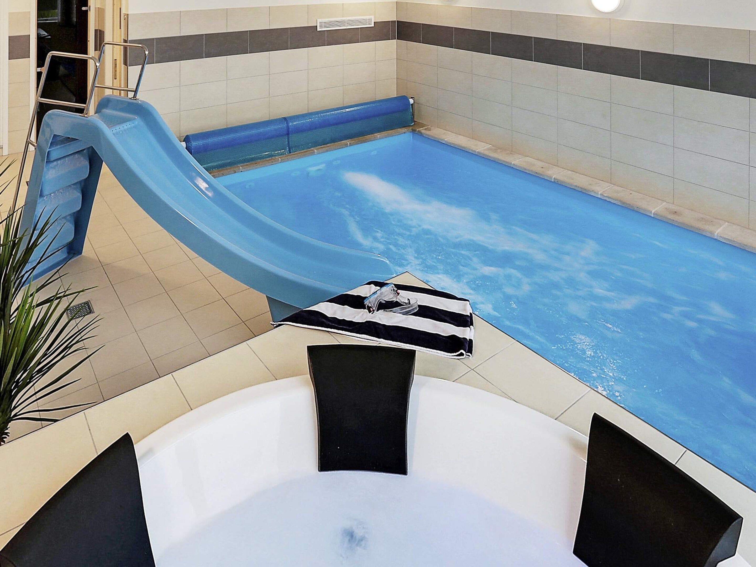 Een binnenzwembad met een blauwe glijbaan, een whirlpool en een klein tafeltje met een handdoek en schoen.