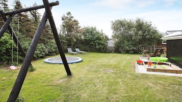 Un patio trasero con un trampolín, un conjunto de columpios y un cobertizo pequeño.