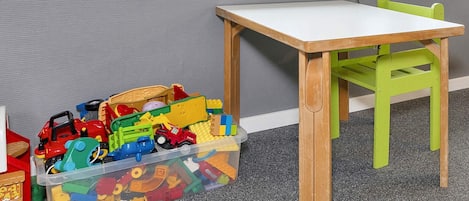 A child's play area with a table and chair, a toy storage bin, and a window with a view.