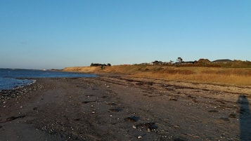 Una playa con cielo despejado, orilla arenosa y una vista distante de una colina con vegetación escasa.