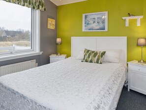 Une chambre à coucher avec un lit, deux tables de chevet, une fenêtre et une vue sur l’extérieur.