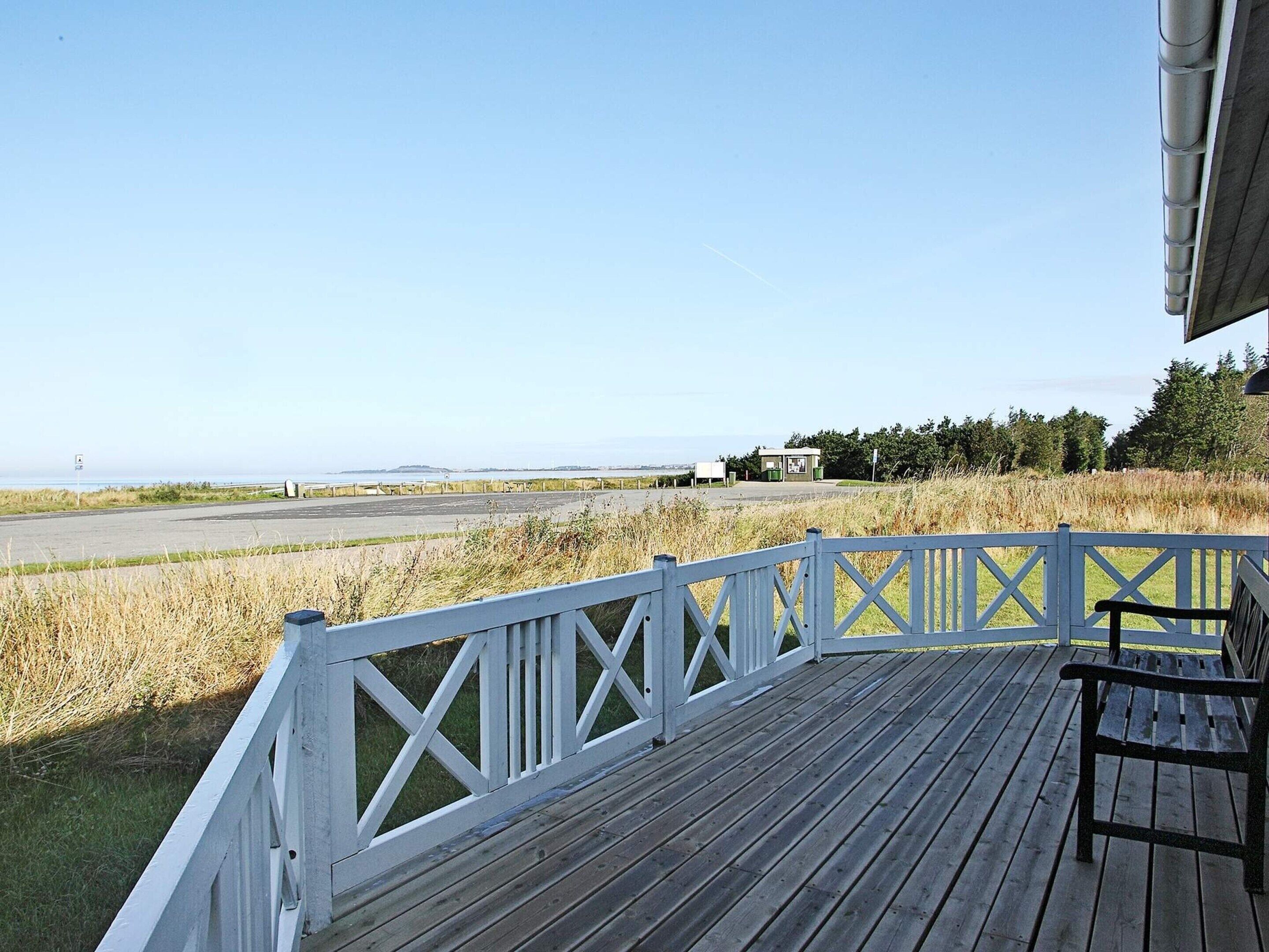 A wooden deck with a white railing overlooking a grassy area and a road.