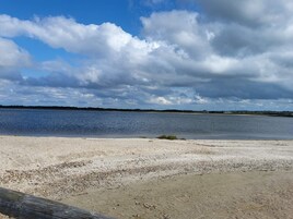 Uma praia com uma cerca de madeira ao primeiro plano e um corpo de água ao fundo.