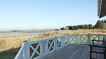 A wooden deck with a white railing overlooking a grassy area and a road.