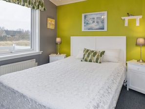 A bedroom with a bed, two bedside tables with lamps, a window, and a green wall with a painting.