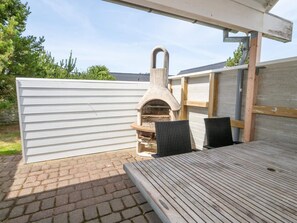 An outdoor patio with a brick floor, a wooden table, two wicker chairs, and a stone-built pizza oven. - 4 Star Holiday Home in Thisted (Thisted)
