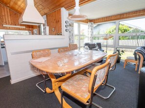 A dining area with a round table and chairs, a kitchen area with a stove and cabinets, and a view of the outdoors through large windows. - 4 Star Holiday Home in Thisted (Thisted)