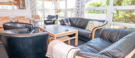 Een gemeubileerde kamer met een bank, stoelen, een tafel en een raam met gordijnen.