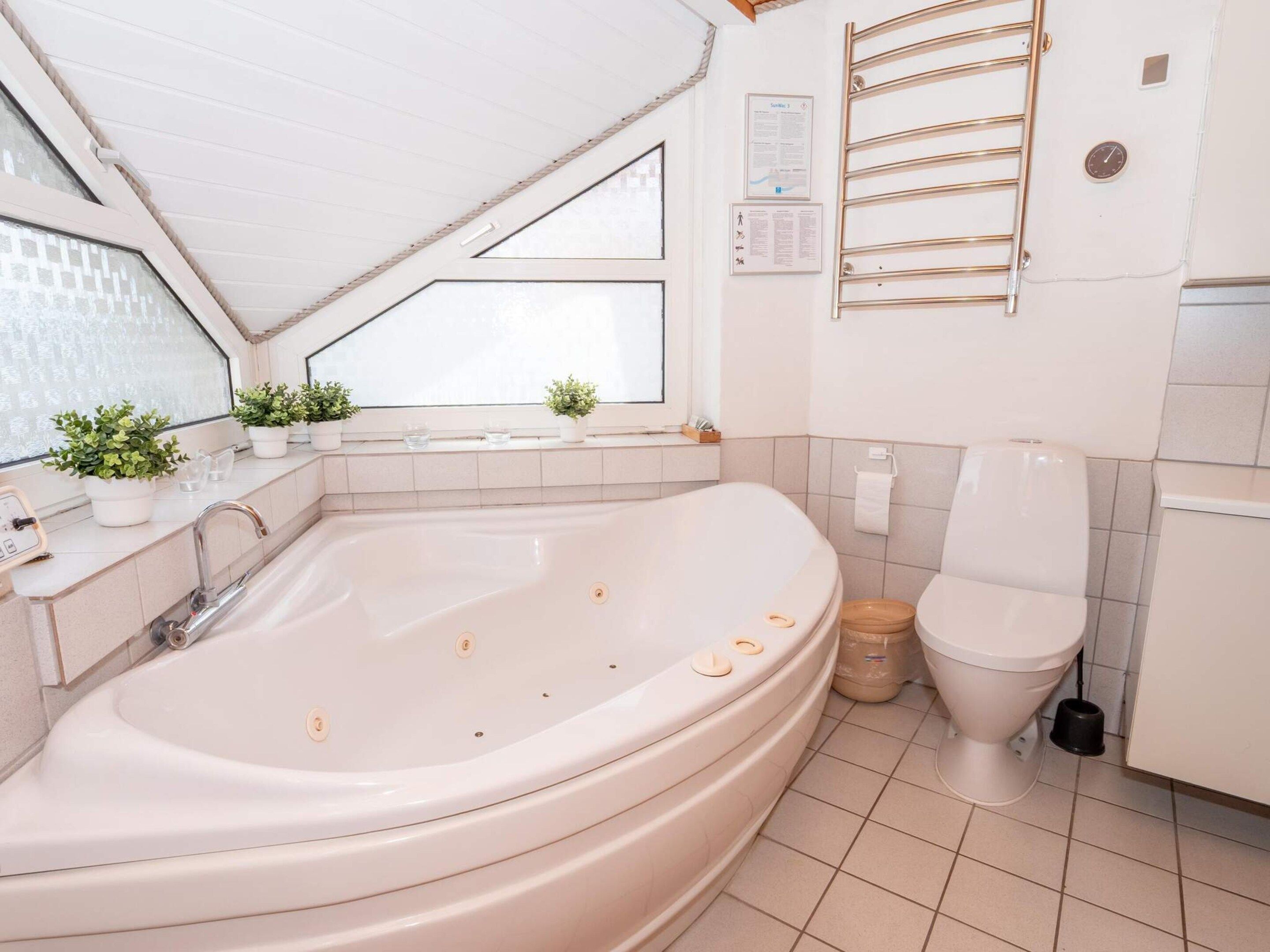A modern bathroom with a freestanding bathtub, a toilet, and a window with potted plants.
