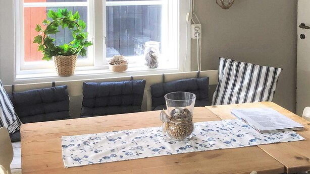A dining area with a wooden table, blue floral tablecloth, and a clear glass pitcher with a plant. - 5 Person Holiday Home in Kungshamn (Kungshamn)