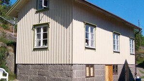 Un bâtiment à deux étages, doté de fondations en pierre, de nombreuses fenêtres avec volets et d’une porte en bois.