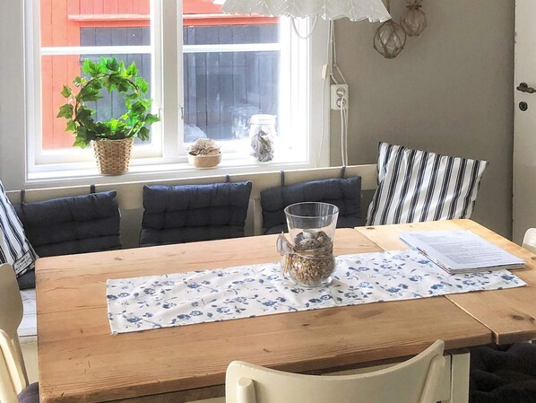 Un comedor con una mesa de madera, mantel floral azul y una jarra de vidrio transparente con una planta.