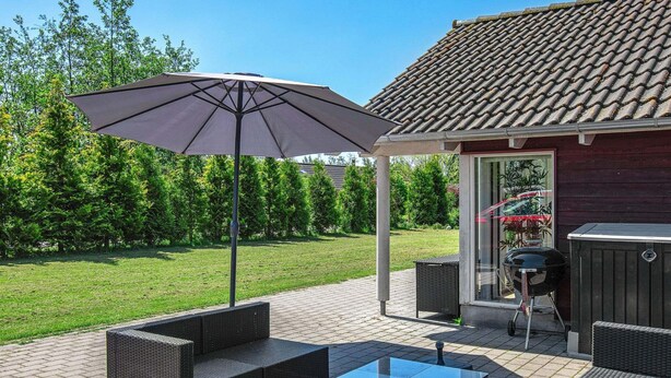 An outdoor patio with wicker furniture, a glass-top table, and a large umbrella. - Wooden Holiday Home in Falster near Sea (Vaeggerlose)