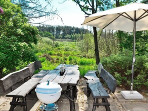 An outdoor dining area with wooden benches and a grill, surrounded by lush greenery and trees. - Modern Holiday Home in Silkeborg With Terrace (Silkeborg)