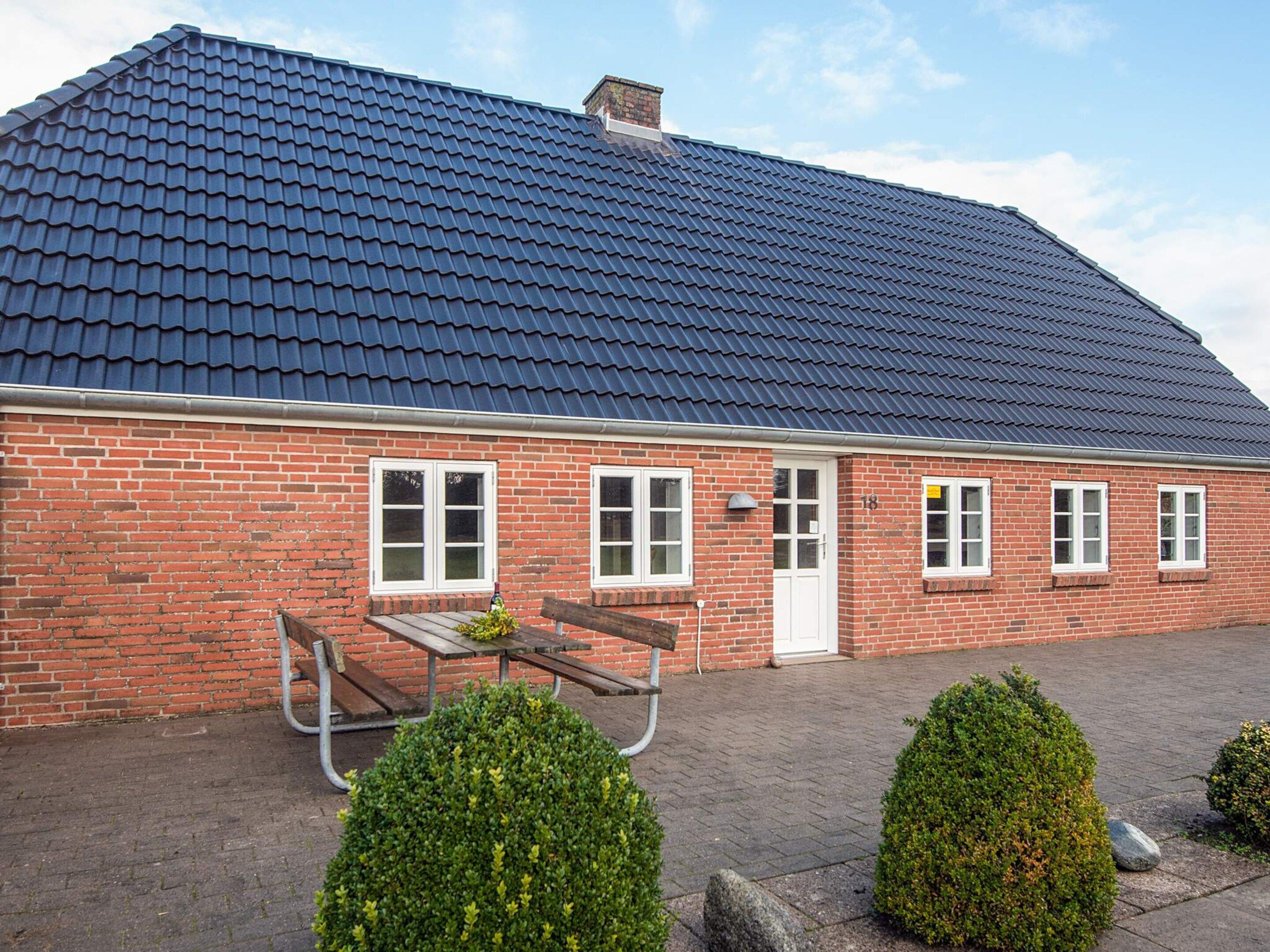 A brick building with a dark tiled roof, a white door, and a bench outside.