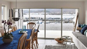 A dining area with a table set for four, a sofa, and a view of a rocky shoreline. - 5 Star Holiday Home in Brattvag (Ålesund)