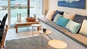 A modern living room with a large window, a sofa with multiple cushions, a small round table, and a wooden coffee table. - 5 Star Holiday Home in Brattvag (Ålesund)