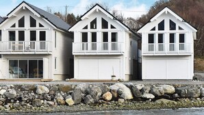 A row of three white, single-story houses with gabled roofs and front porches, situated next to a rocky shoreline. - 5 Star Holiday Home in Brattvag (Ålesund)