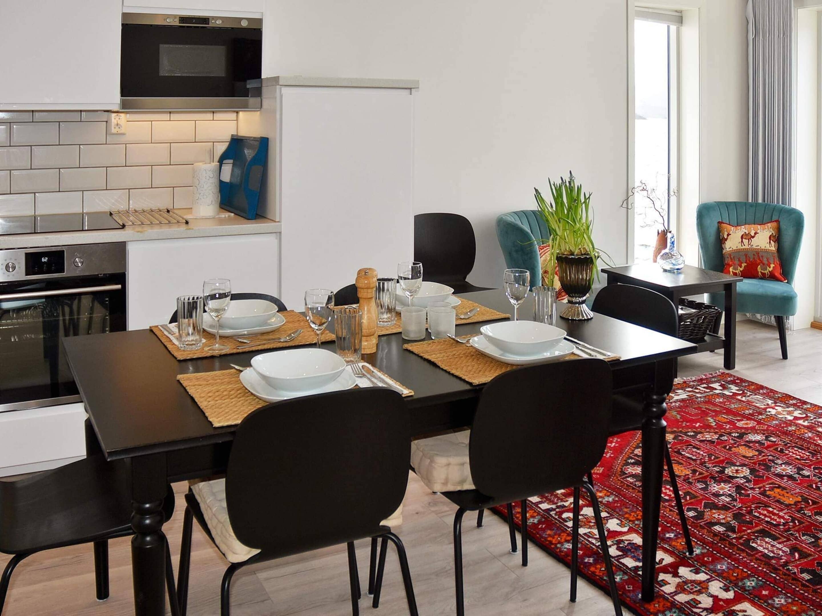 Una cucina moderna con forno a microonde, forno e zoccolo di piastrelle bianche. È presente un tavolo da pranzo apparecchiato con piatti, bicchieri e una pianta.
