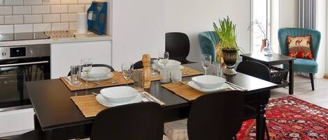A modern kitchen with a microwave, oven, and white tiled backsplash. There is a dining table set with plates, glasses, and a plant.