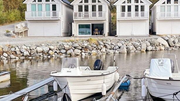 A row of white cabins with balconies, a dock with boats, and a rocky shoreline. - 5 Star Holiday Home in Brattvag (Ålesund)