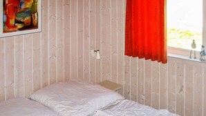A room with two single beds, a wooden wall, a window with a red curtain, and a wall-mounted light fixture. - Holiday Home in Otterndorf (Otterndorf)