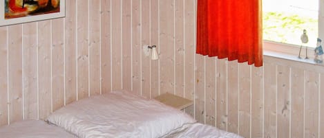 Una habitación con dos camas individuales, una pared de madera, un ventanal con cortina roja y una lámpara fijada a la pared.