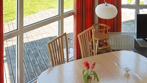 A room with a round table, two wooden chairs, a potted plant, and a window with a view of a wooden deck. - Holiday Home in Otterndorf (Otterndorf)