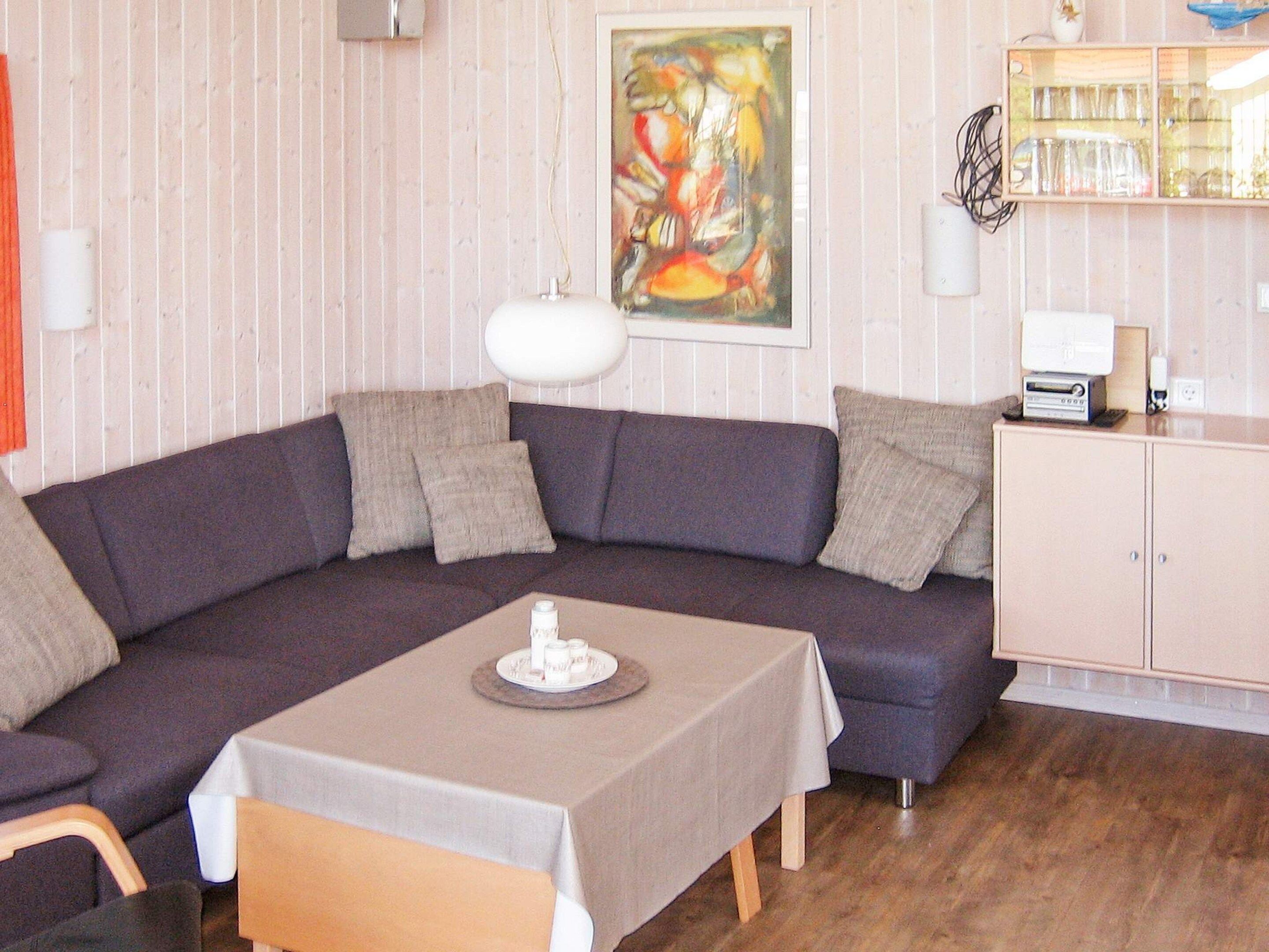 A room with a dark-colored sofa, a small table with a white tablecloth, a painting on the wall, and a cabinet with glassware.