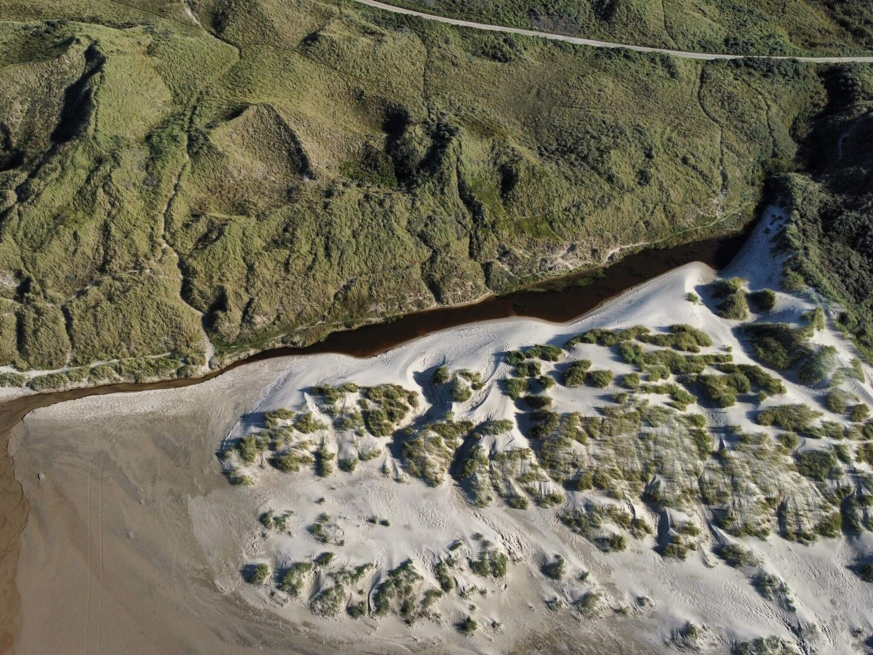 An aerial view of a coastal landscape with a road, sandy dunes, and dense vegetation.