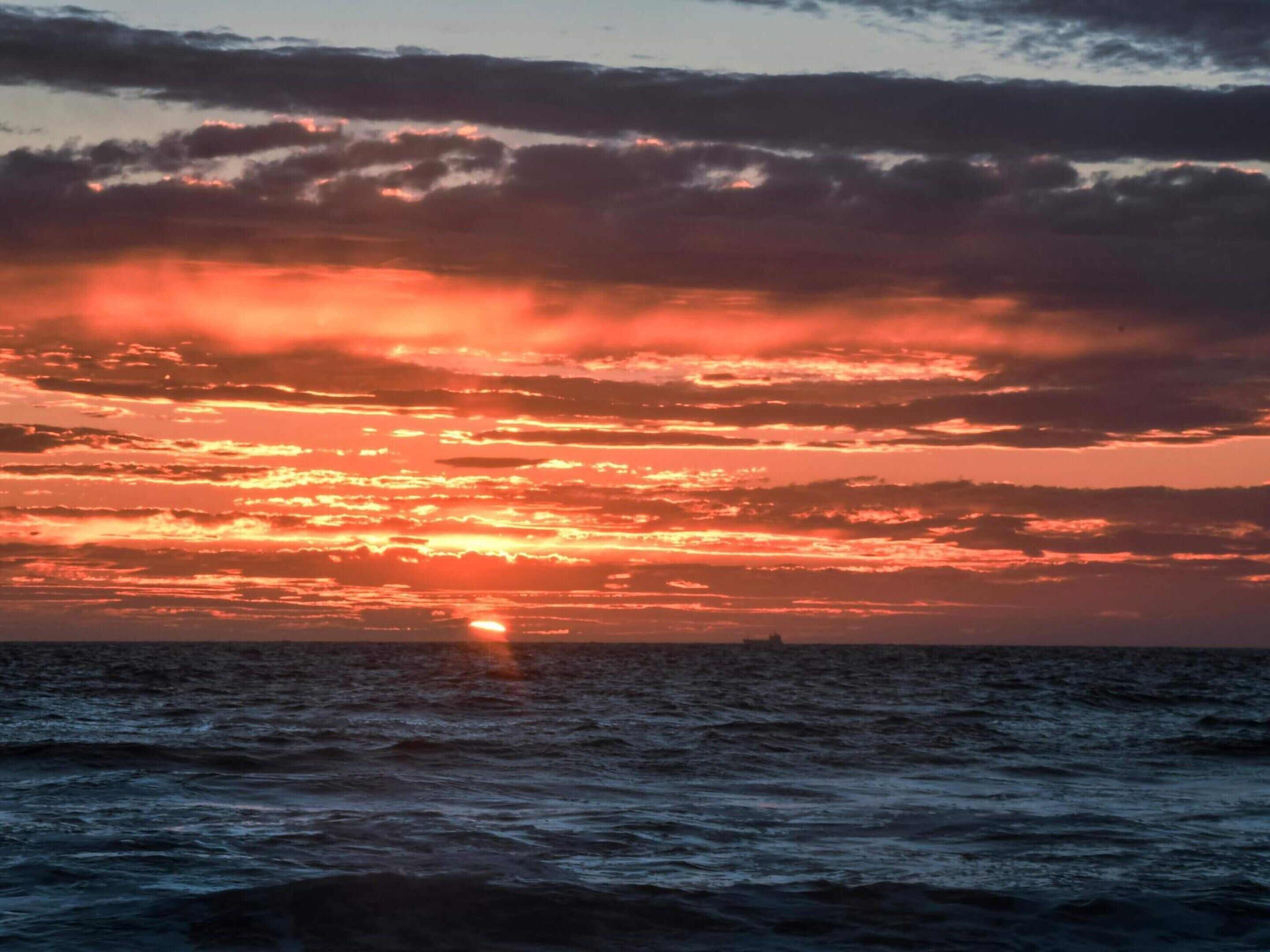 En solnedgång över havet med moln på himlen.