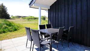 Un patio al aire libre con una mesa y sillas, un pilar blanco y vistas a un campo cubierto de césped.