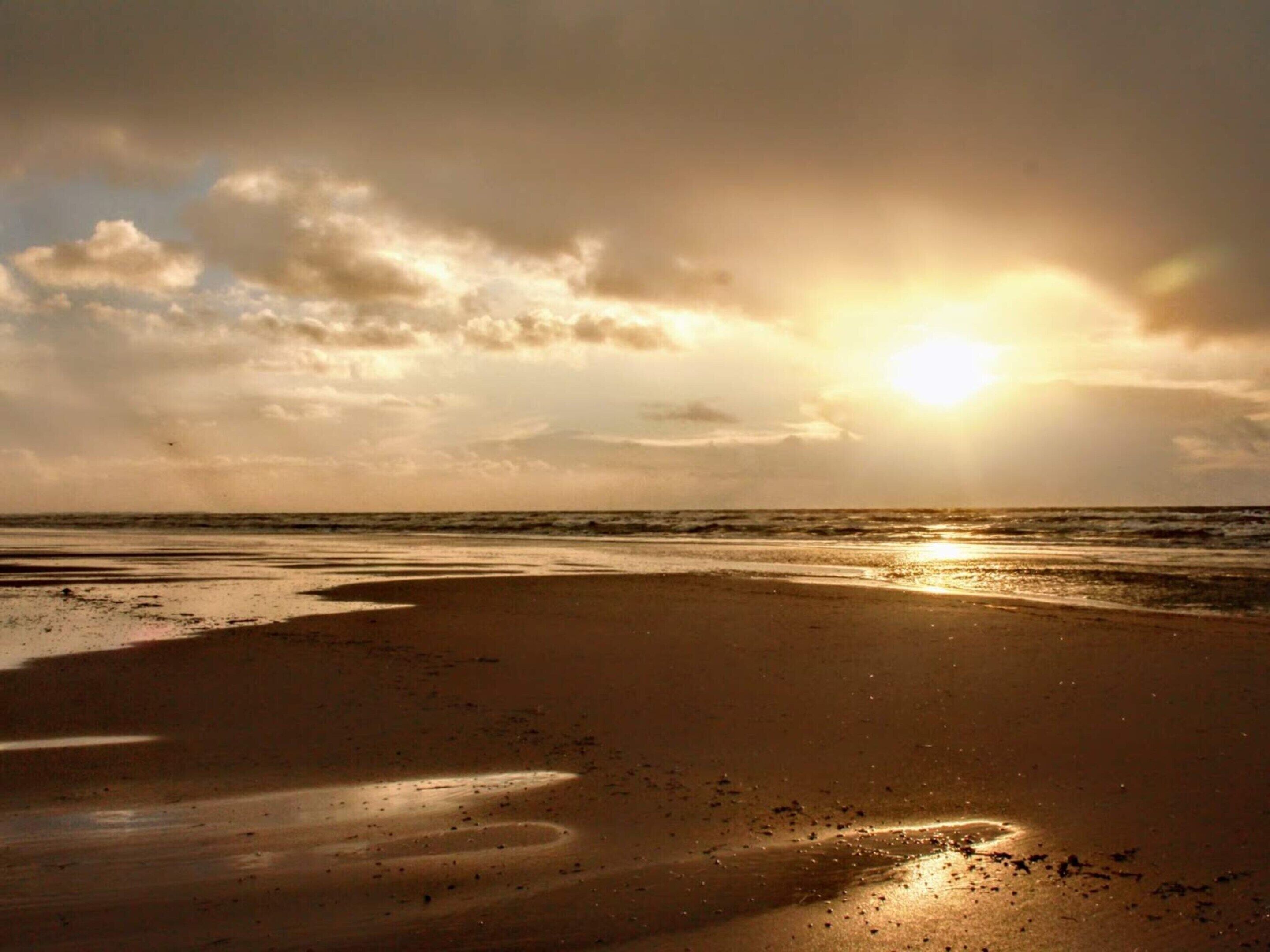 A beach with the sun setting over the horizon, creating a silhouette of the landscape.