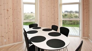 Un comedor moderno con una mesa blanca, sillas negras, ventanas amplias y paredes de madera.