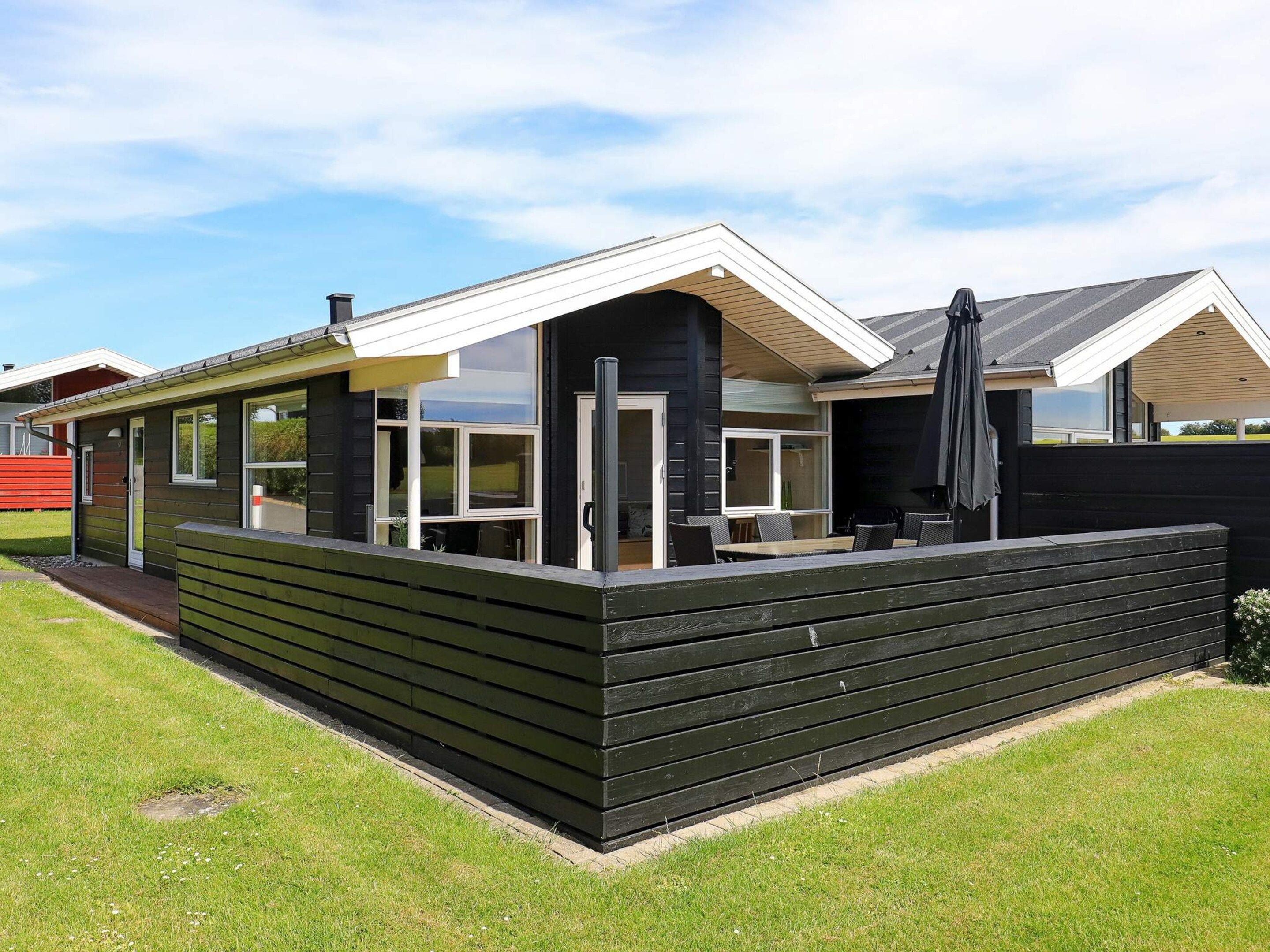 A modern house with a covered patio, large windows, and a black exterior.