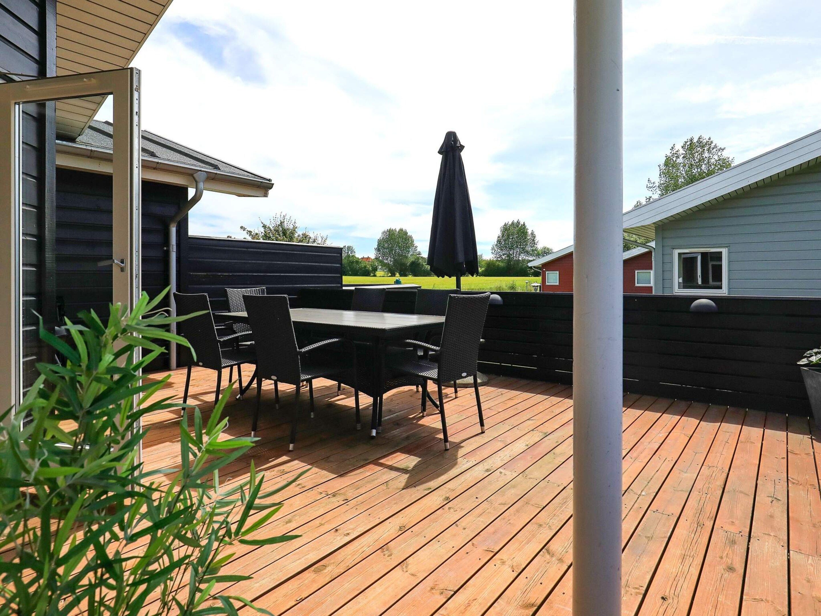 An outdoor patio with a table and chairs, a black umbrella, and a view of a green field.