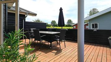 An outdoor patio with a table and chairs, a black umbrella, and a view of a green field.