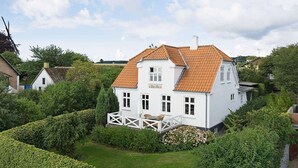 A white house with a tiled roof, surrounded by well-maintained hedges and a lawn. - Quaint Holiday Home in Bornholm near Sea (Svaneke)