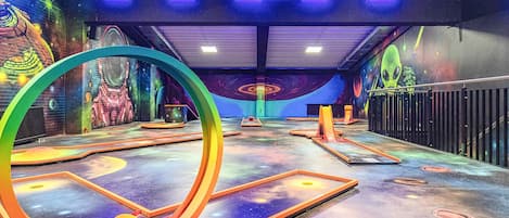 Un espace de jeux intérieur agrémenté de peintures murales colorées, d’une grande structure circulaire et de divers équipements de jeux.