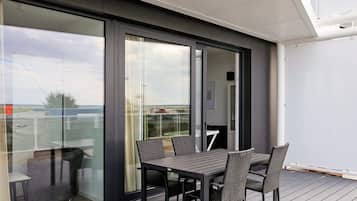 Un espacio moderno para comer al aire libre con mesa y sillas, una puerta de cristal que da a un balcón y vistas al cielo y un paisaje lejano.