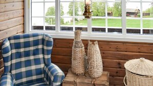 Ein Karo-Sessel an einem Holzfenster mit Blick auf ein grünes Feld.