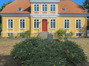Un bâtiment jaune avec une porte rouge, de nombreuses fenêtres et un toit rouge.