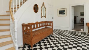 A staircase with white balusters and wooden steps, a wooden bench, a black and white checkered floor, a white door, and a framed mirror on the wall. - Vintage Holiday Home in Syddanmark With Private Whirlpool (Sydlangeland)