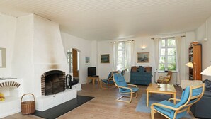 A spacious living room with a fireplace, wooden flooring, and a seating area with blue chairs and a sofa. - Vintage Holiday Home in Syddanmark With Private Whirlpool (Sydlangeland)