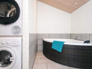 A compact bathroom with a washing machine, a bathtub, and a towel hanging on the wall.