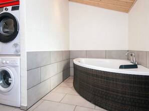 A modern bathroom with a built-in washing machine, a freestanding bathtub, and tiled walls.
